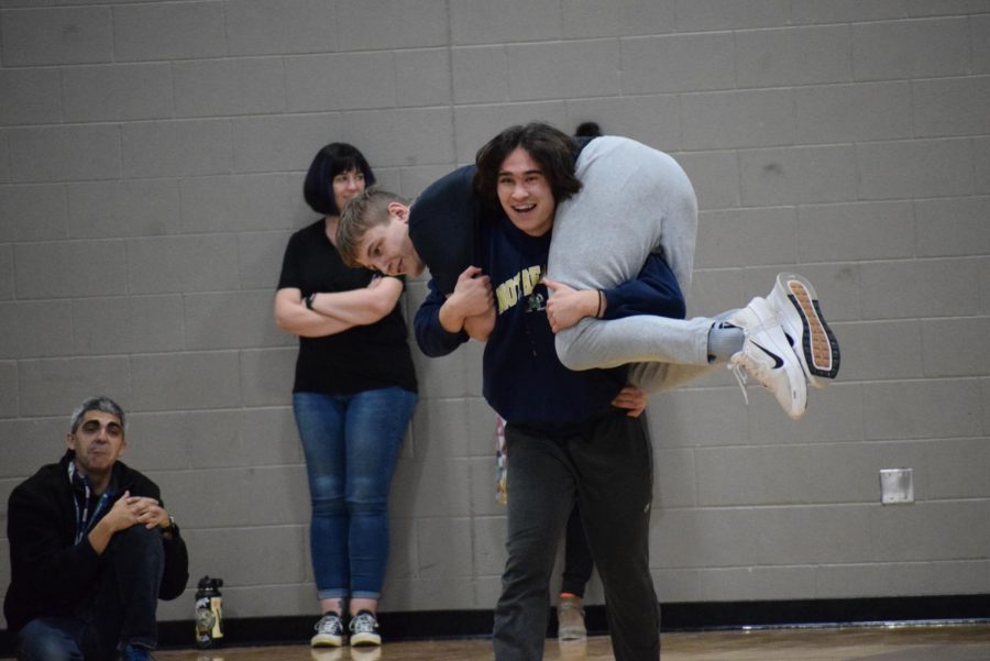 Representing the wrestling team, Misha Byers (12) carries Logan Noble (12) in a firemans carry at the winter assembly during the marine corp drill contest. 
